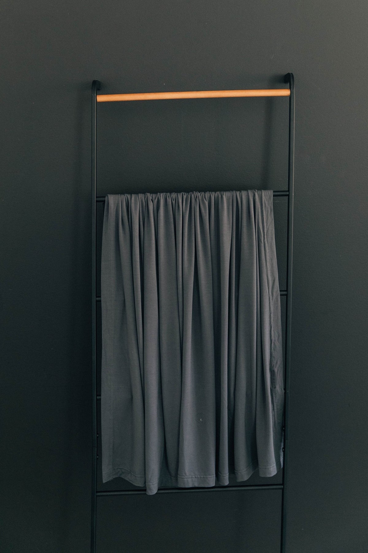 Charcoal-colored fabric draped over a black metal rack against a dark wall, showcasing minimalist home decor style.