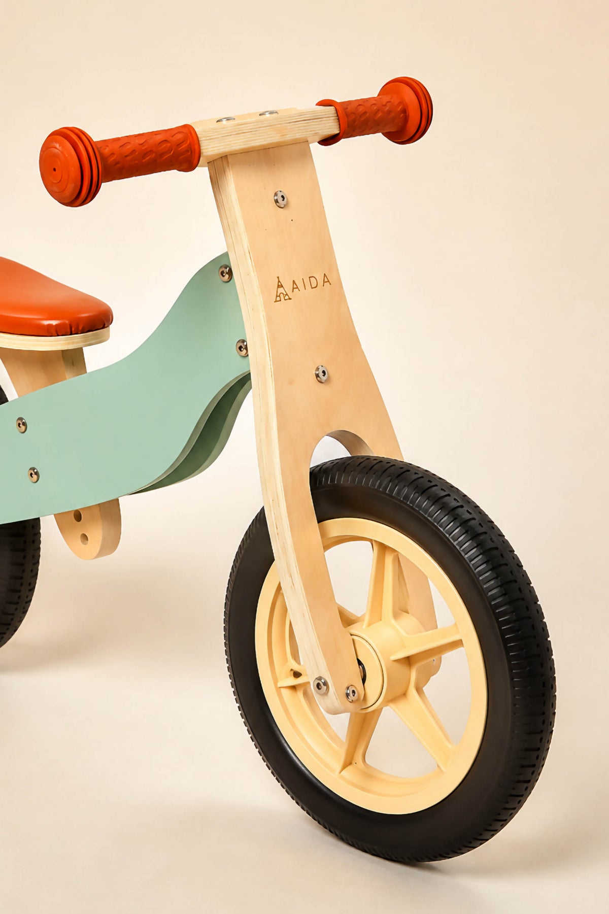 A wooden balance bike features a mint green frame, orange seat, and red handlebars. Designed for children aged 3 to 5, it emphasizes balance and coordination in a sustainable style.