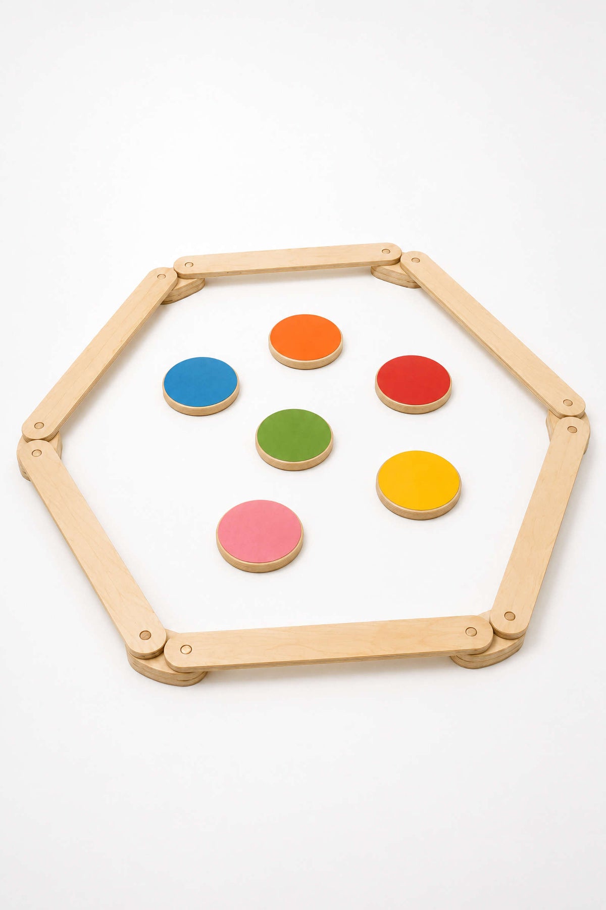 A hexagon-shaped wooden frame surrounds colorful, circular stepping stones in vibrant red, green, pink, yellow, and blue. This sustainable play set encourages creative movement and coordination for children.