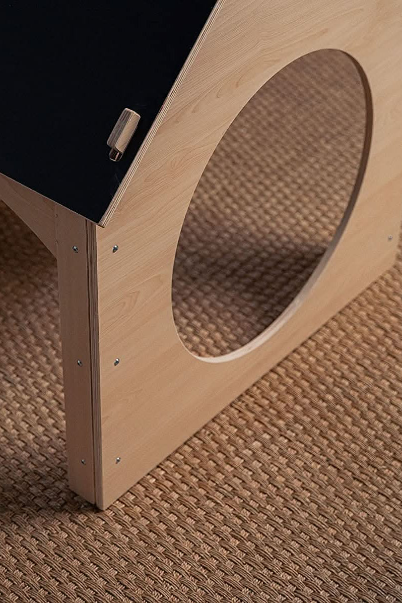 A close-up view of a wooden childrens playhouse featuring a chalkboard roof, set on a textured, woven rug. The natural wood finish highlights its eco-friendly design and playful aesthetic.