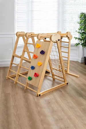 Wooden foldable jungle gym with colorful climbing holds in a bright room with wooden floors and a green plant.