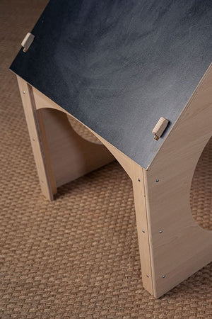 A wooden childrens playhouse features a chalkboard roof and circular openings for play. Its natural finish and sturdy design encourage imaginative play in a cozy setting.