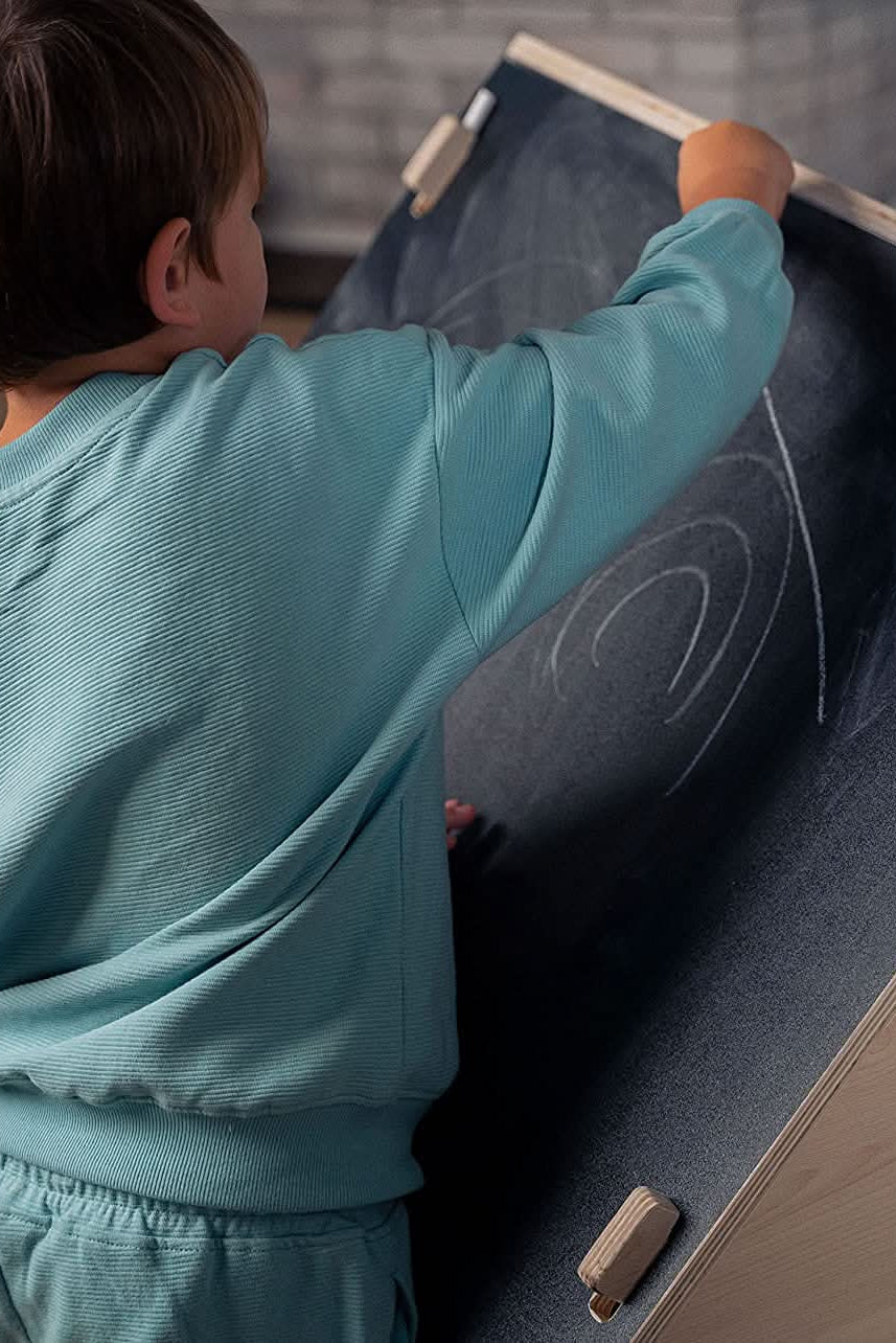 Two children actively drawing on a double-sided chalkboard easel, showcasing their creativity. The easel features a natural wooden frame, designed for imaginative play in a cozy indoor setting.