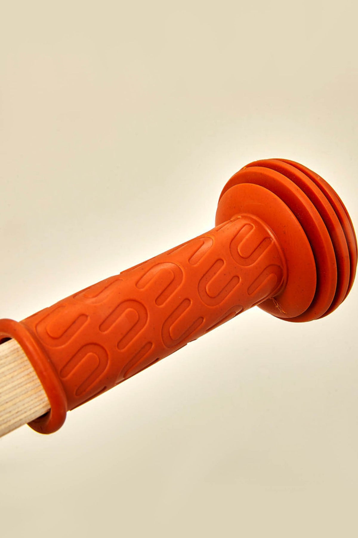 Close-up of a textured, orange rubber handle featuring grooves, attached to a wooden frame. This component appears to enhance grip and comfort for young children using the balance bike.