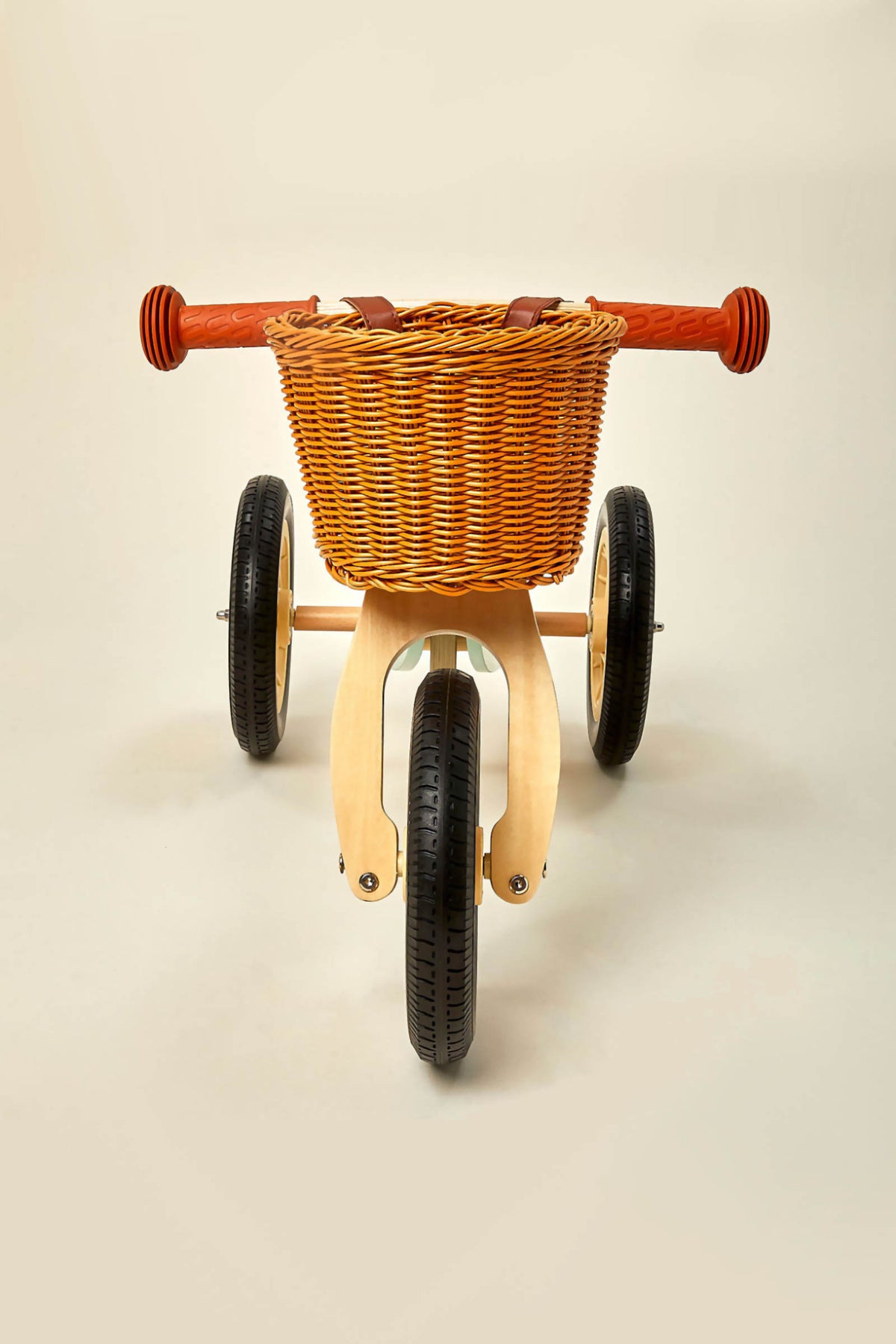 A wooden balance bike with a woven basket and bright orange handlebars is shown against a neutral background. This eco-friendly design is perfect for toddlers aged 2 to 4 years.