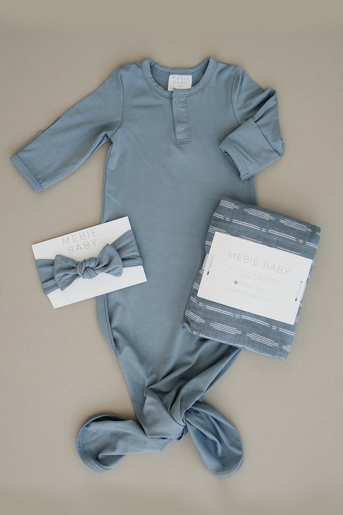 Dusty blue baby gown, head wrap, and swaddle set made from soft bamboo fabric, displayed on a neutral background.