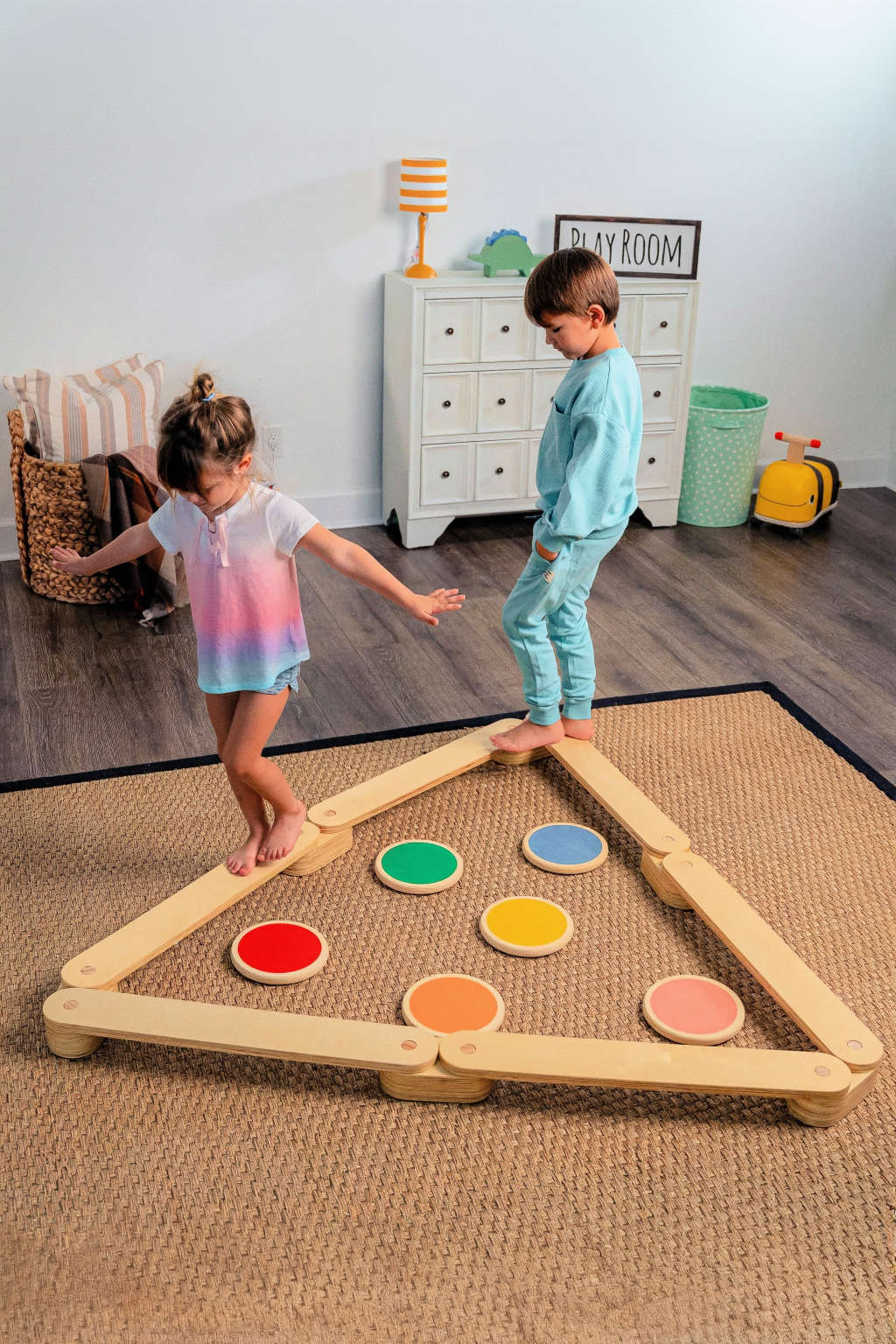 Two children play on a wooden balance beam and stepping stones set, featuring colorful circular stones in a triangular layout.