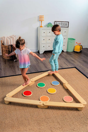 Two children play on a wooden balance beam and stepping stones set, featuring colorful circular stones in a triangular layout.