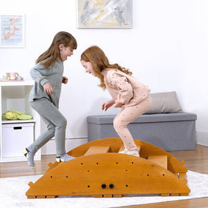 Two children joyfully play on a wooden rocker climber, smiling as they jump off its curved surface. The playset is made of sustainably sourced wood, promoting active, imaginative play.