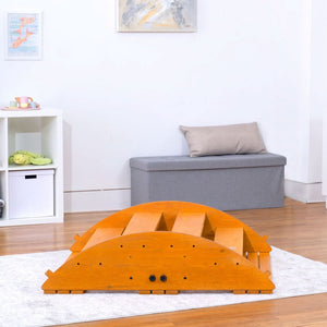 A wooden Jumbo Rocker and Climber in a warm honey finish is displayed in a bright playroom with a soft rug, showcasing its dual-function design for active play and exploration.