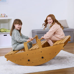 Two children joyfully play on the Banyan Jumbo Rocker, a sustainably crafted wooden climbing toy, in a bright, cozy indoor setting with light-colored flooring.