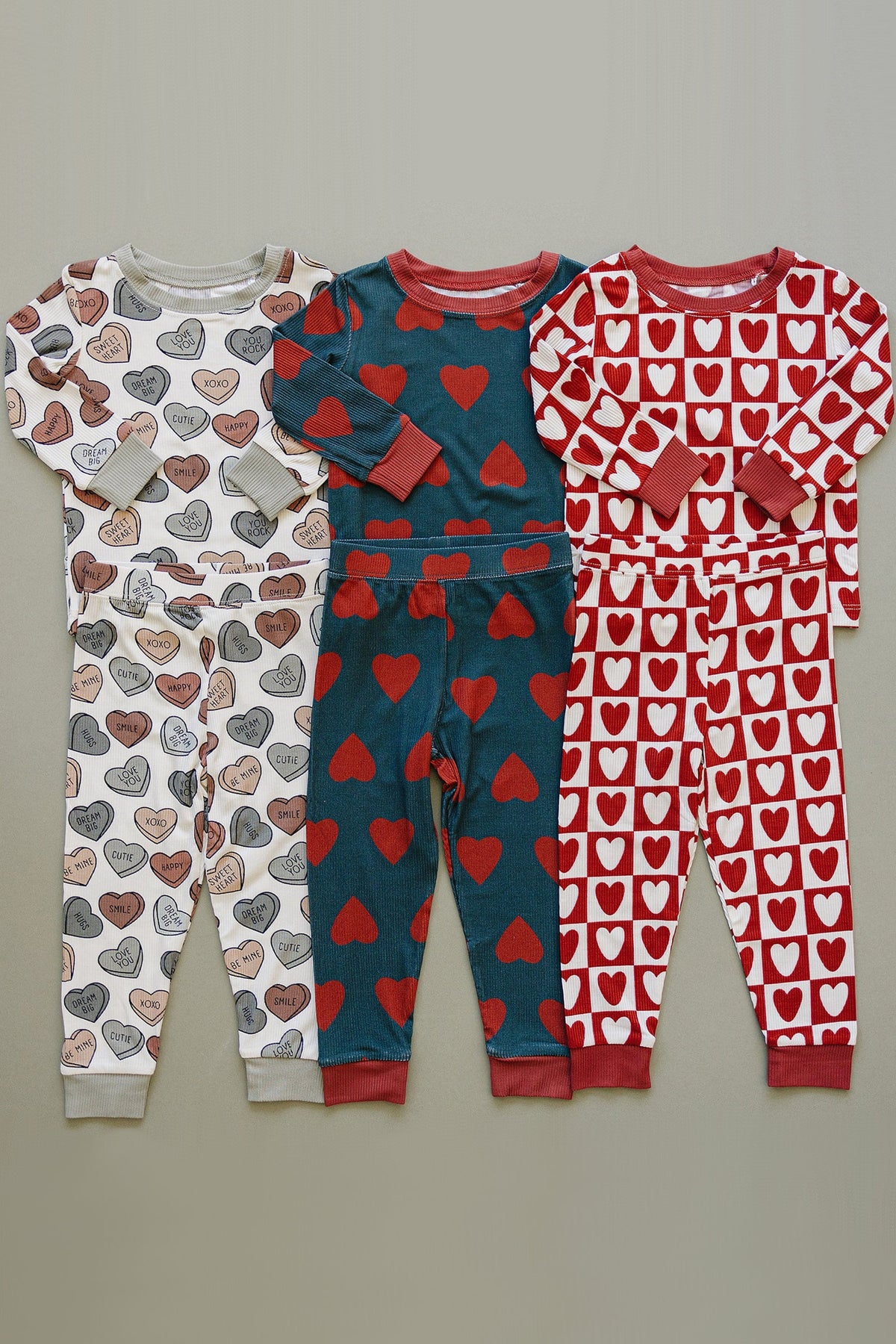 A collection of three cozy pajama sets featuring heart patterns in navy, red, and cream, made from soft bamboo fabric.