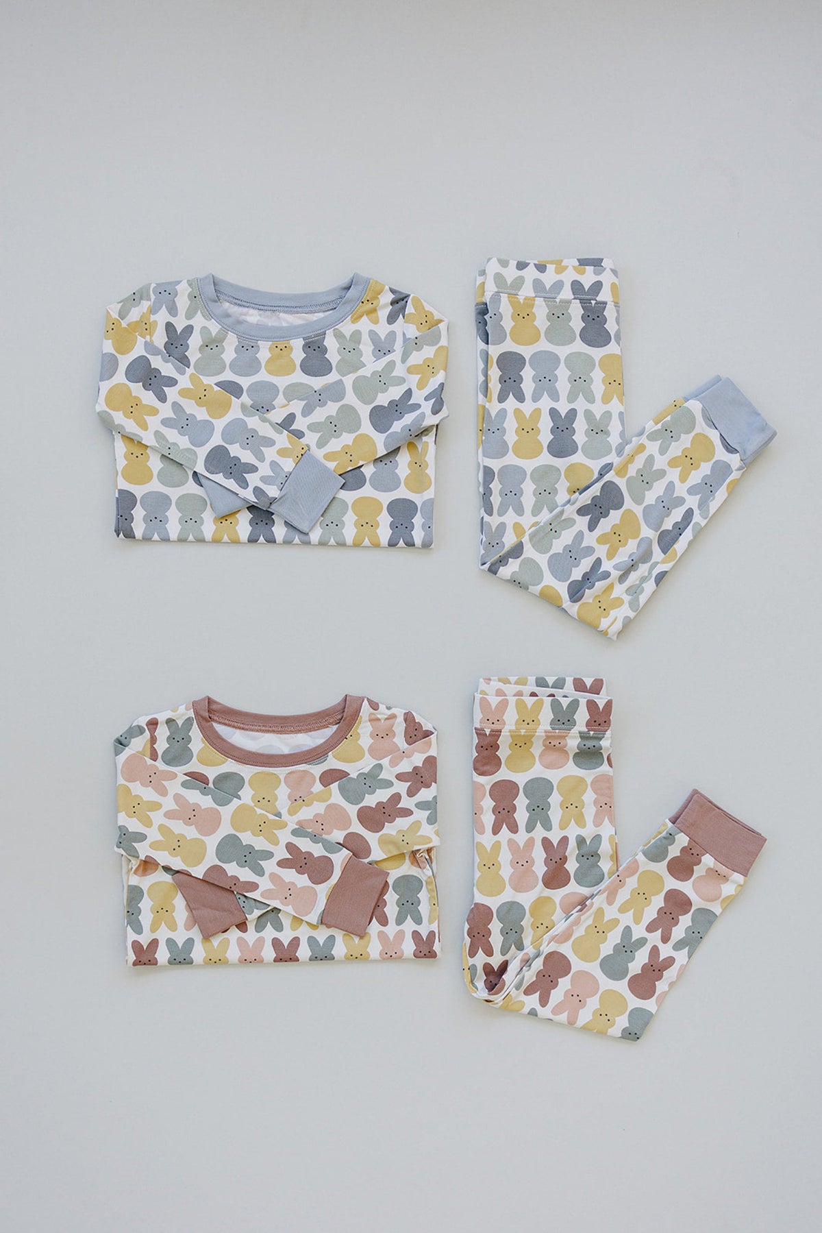 Two sets of childrens pajamas with playful bunny patterns, featuring pastel colors and contrasting cuffs, laid flat.