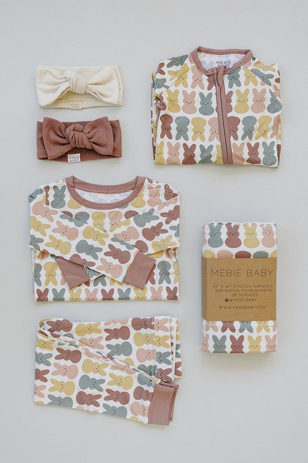 Mebie Baby pajama set and swaddle with pastel bunny print, accompanied by two headbands, on a light background.