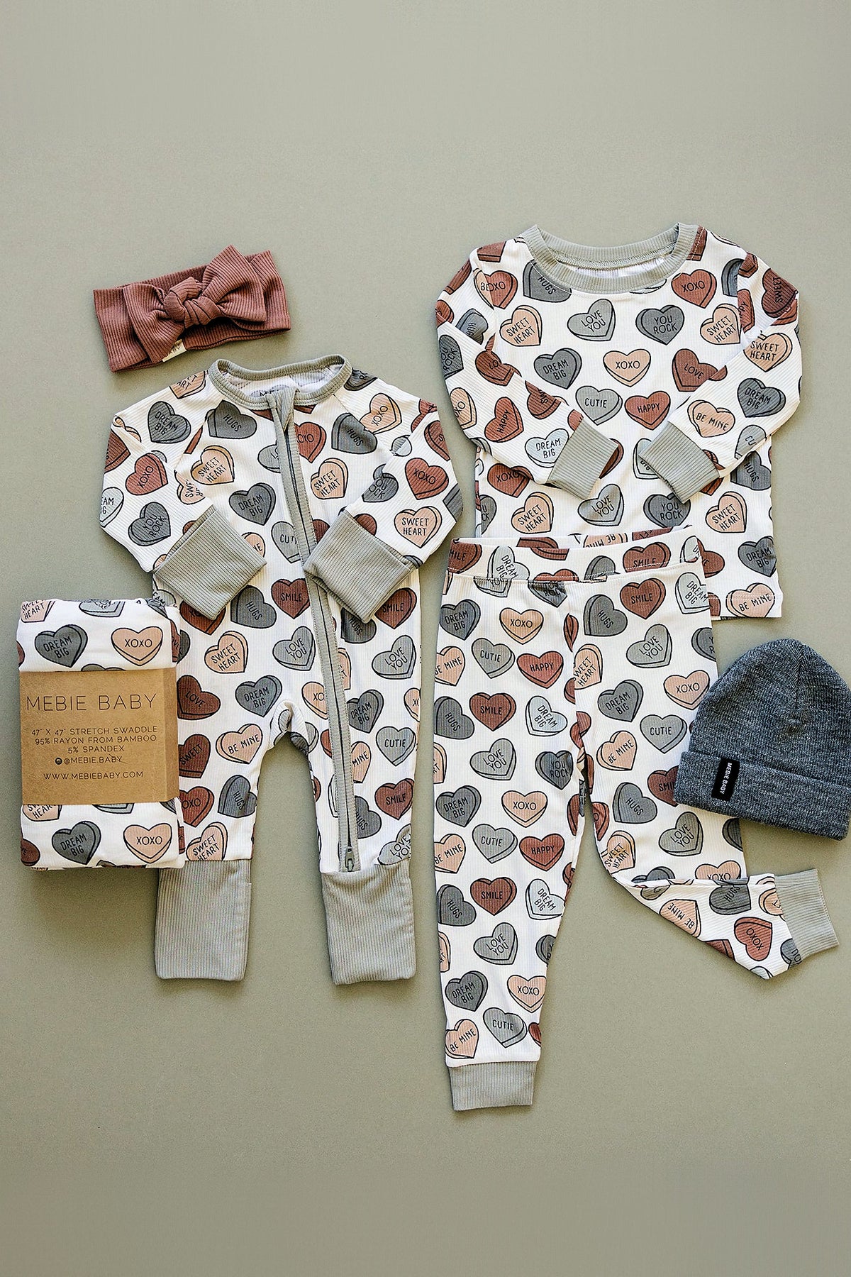 A cozy pajama set for babies featuring a heart print, made from bamboo fabric, accompanied by a headband and hat.