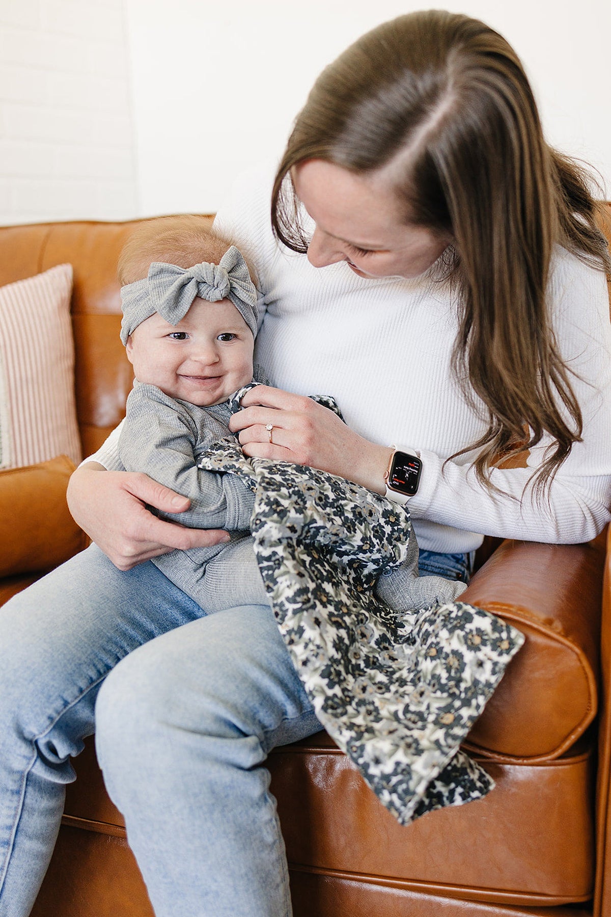 A smiling baby in a gray outfit with a matching headband is held by a person with a floral cloth.