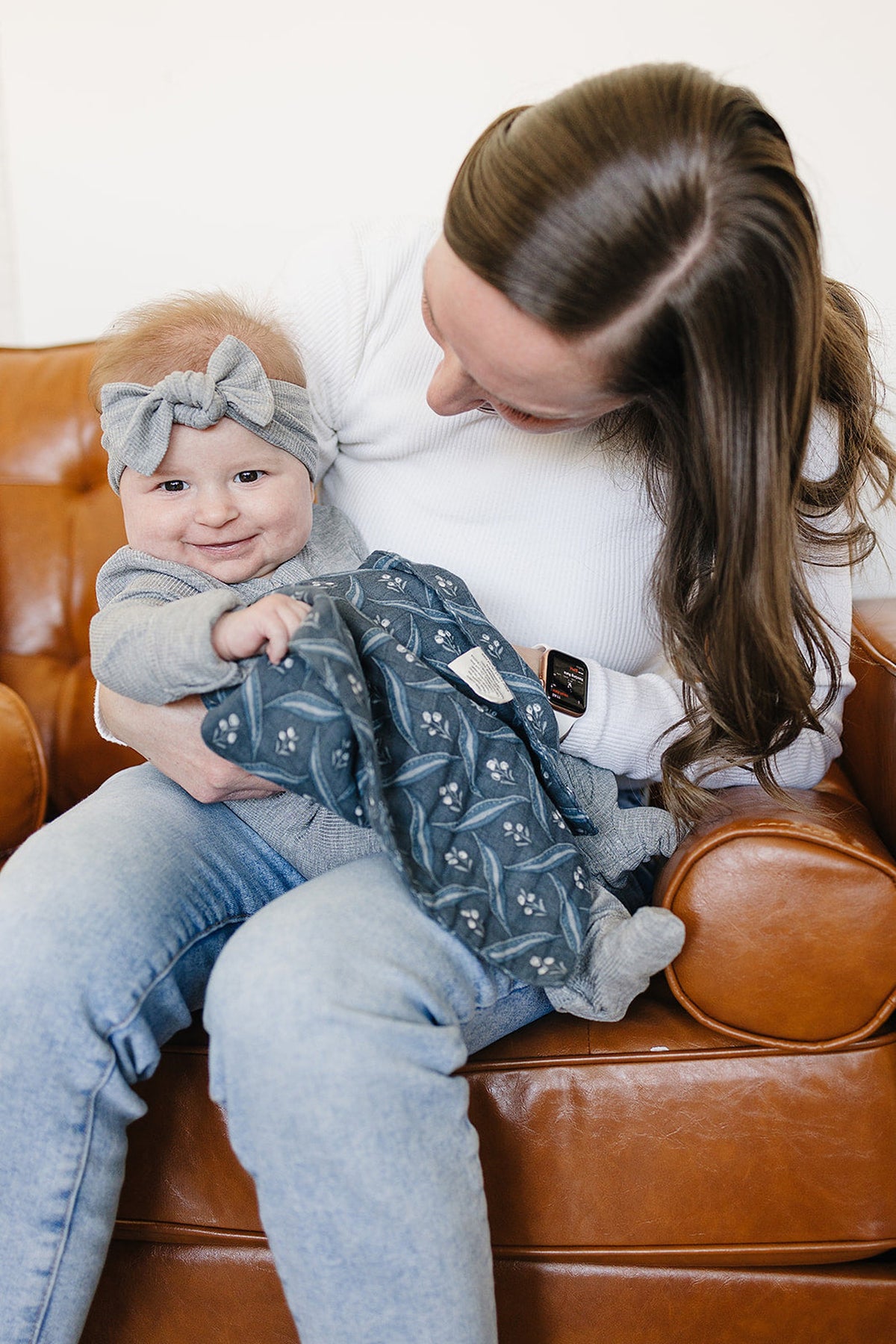 A smiling baby with a gray headband is held by an adult, holding a navy patterned cloth.