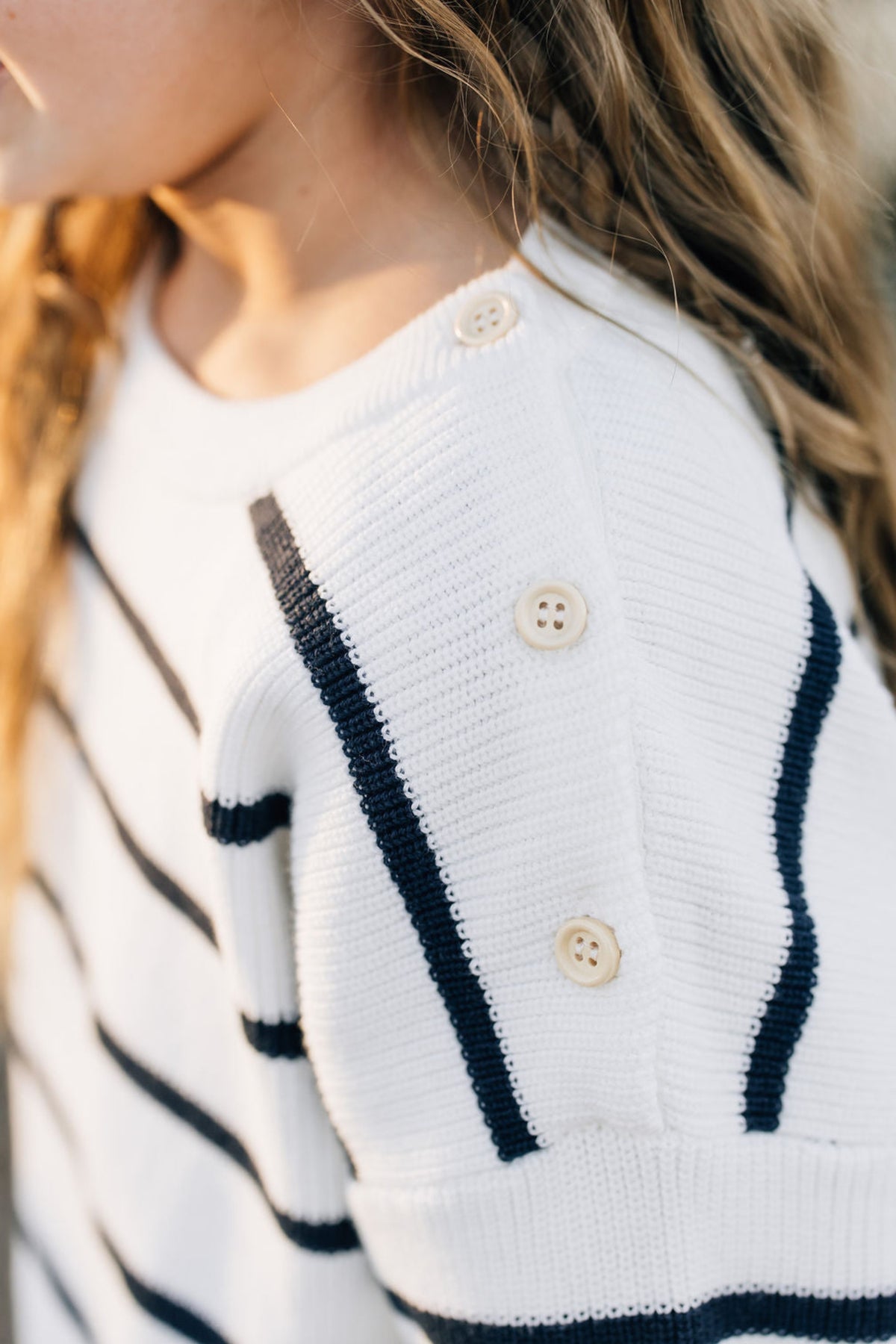 Close-up of a childs white sweater with navy stripes and beige buttons on the shoulder.