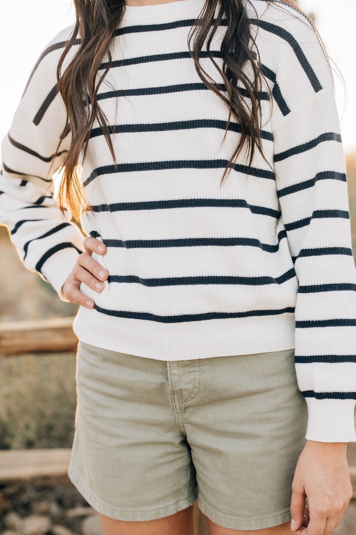 A person wearing a navy and white striped knit sweater with light khaki shorts, standing outdoors.