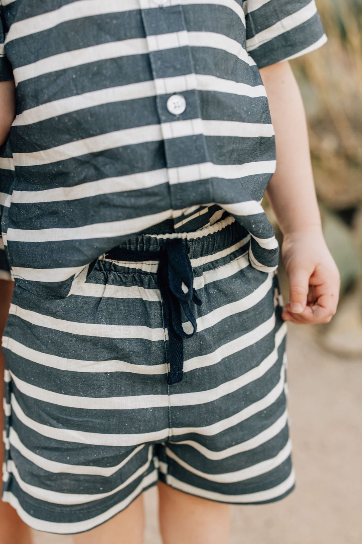 A child wearing navy and white striped linen shorts and a matching shirt, with a drawstring waistband.