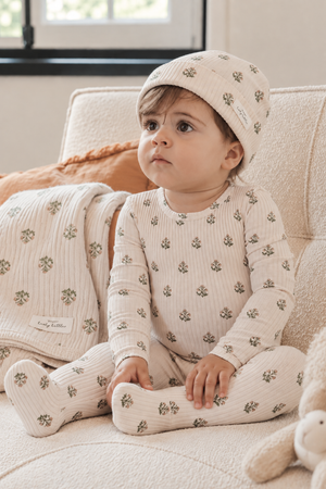 A toddler sits on a cozy sofa, wearing a light-colored, floral-patterned outfit and matching hat. The soft, ribbed fabric adds texture, creating a warm and inviting atmosphere.