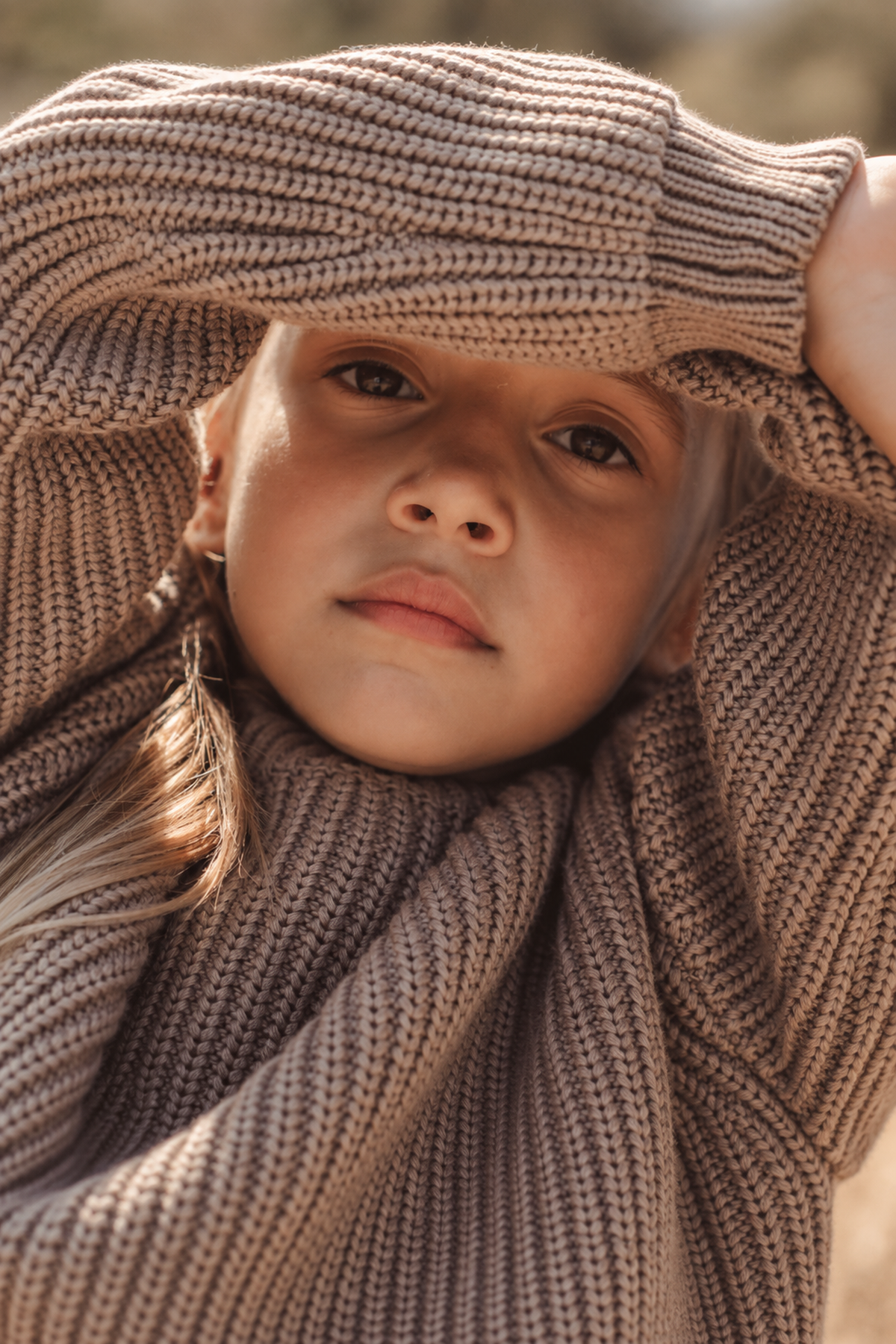 A close-up of a child wearing a chunky knit sweater in a warm beige color, showcasing a relaxed fit and textured fabric.