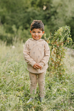 A child wearing a beige cactus-patterned long-sleeve hooded set stands smiling in a grassy outdoor area.