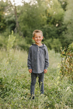 A child in a navy hooded set with lightning bolt patterns stands smiling in a lush, green field.