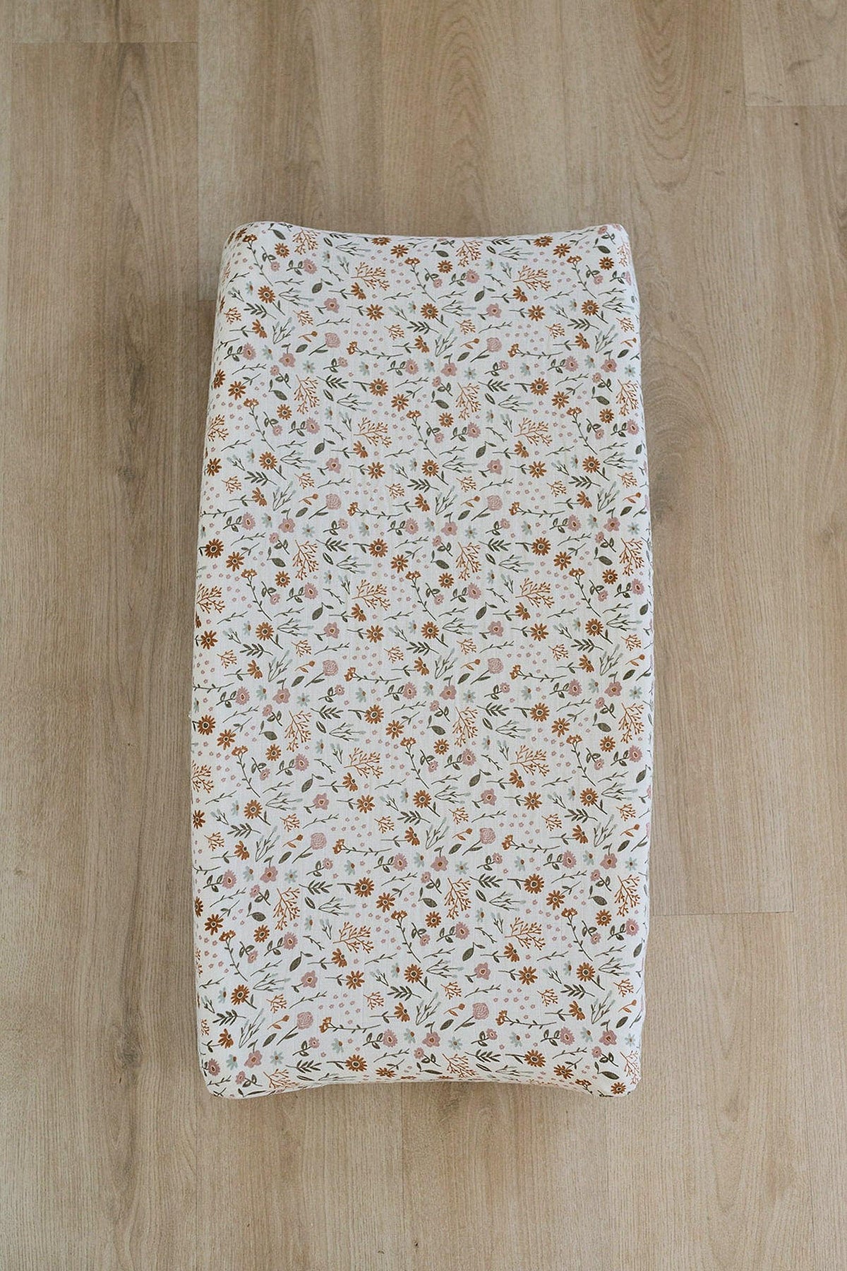 Floral patterned muslin changing pad cover on a wooden floor, featuring delicate flowers in soft pink.