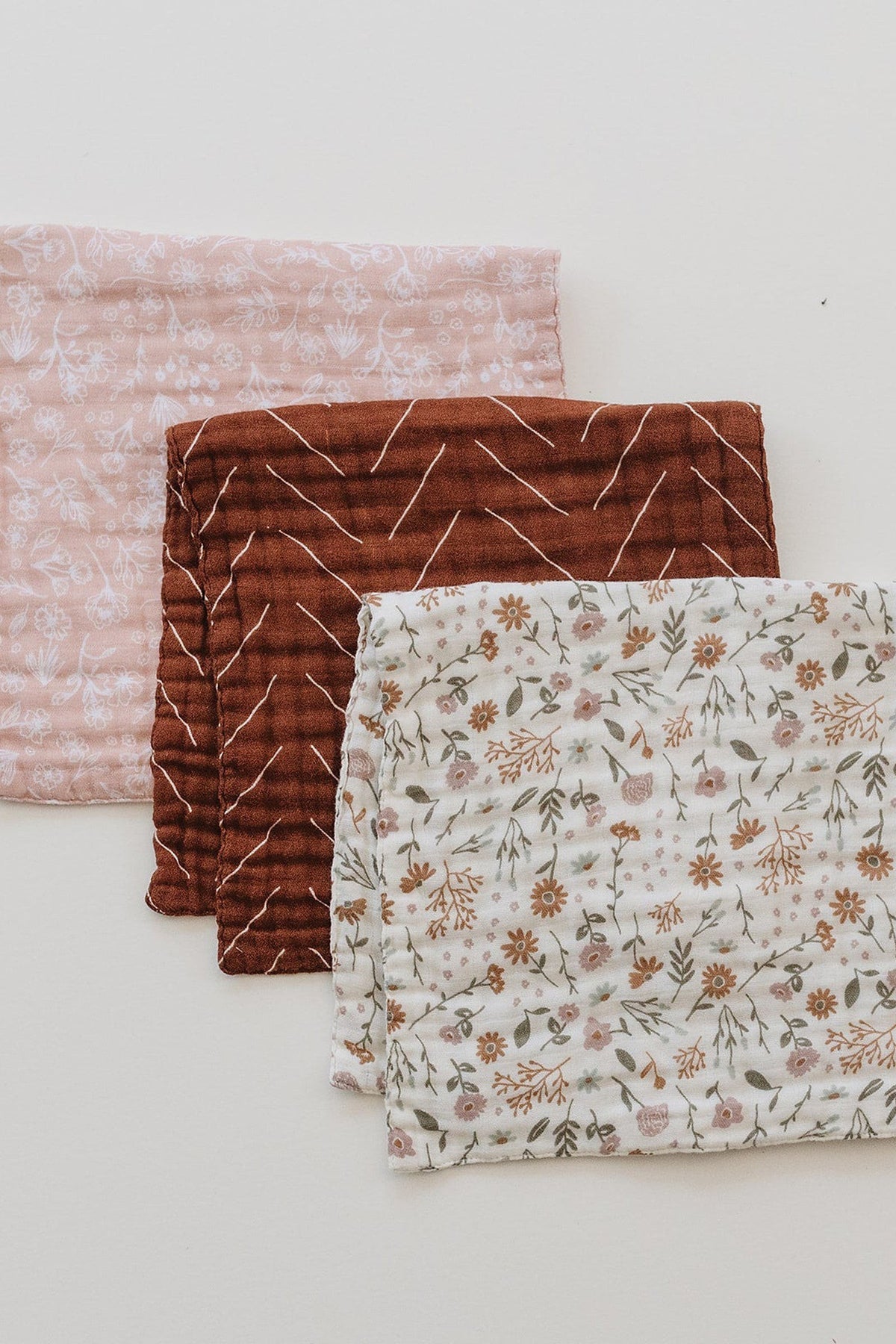 Three burp cloths with floral, rust, and zigzag patterns on soft fabric, arranged on a white background.