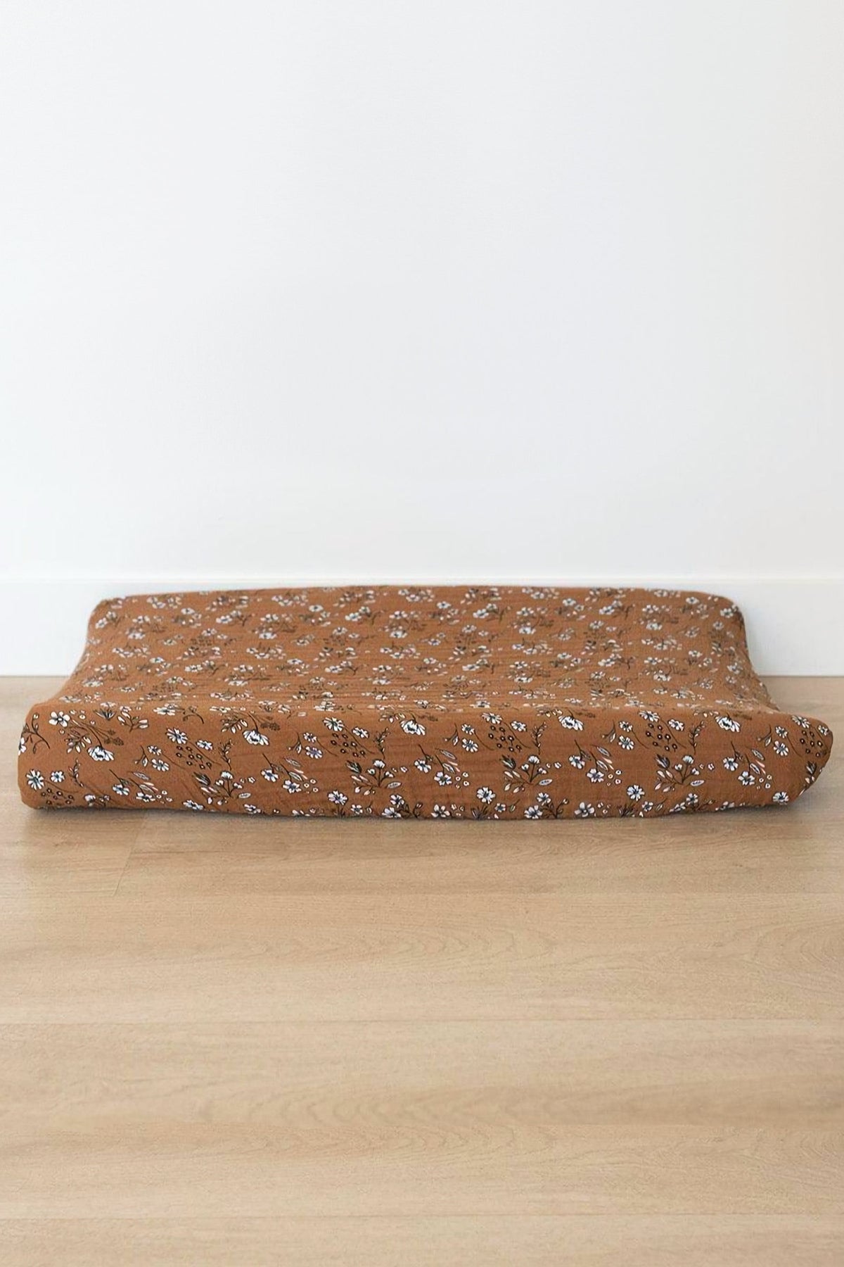 Brown changing pad cover with white floral pattern on a wooden floor, made from soft muslin fabric.
