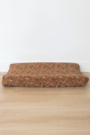 Brown changing pad cover with white floral pattern on a wooden floor, made from soft muslin fabric.