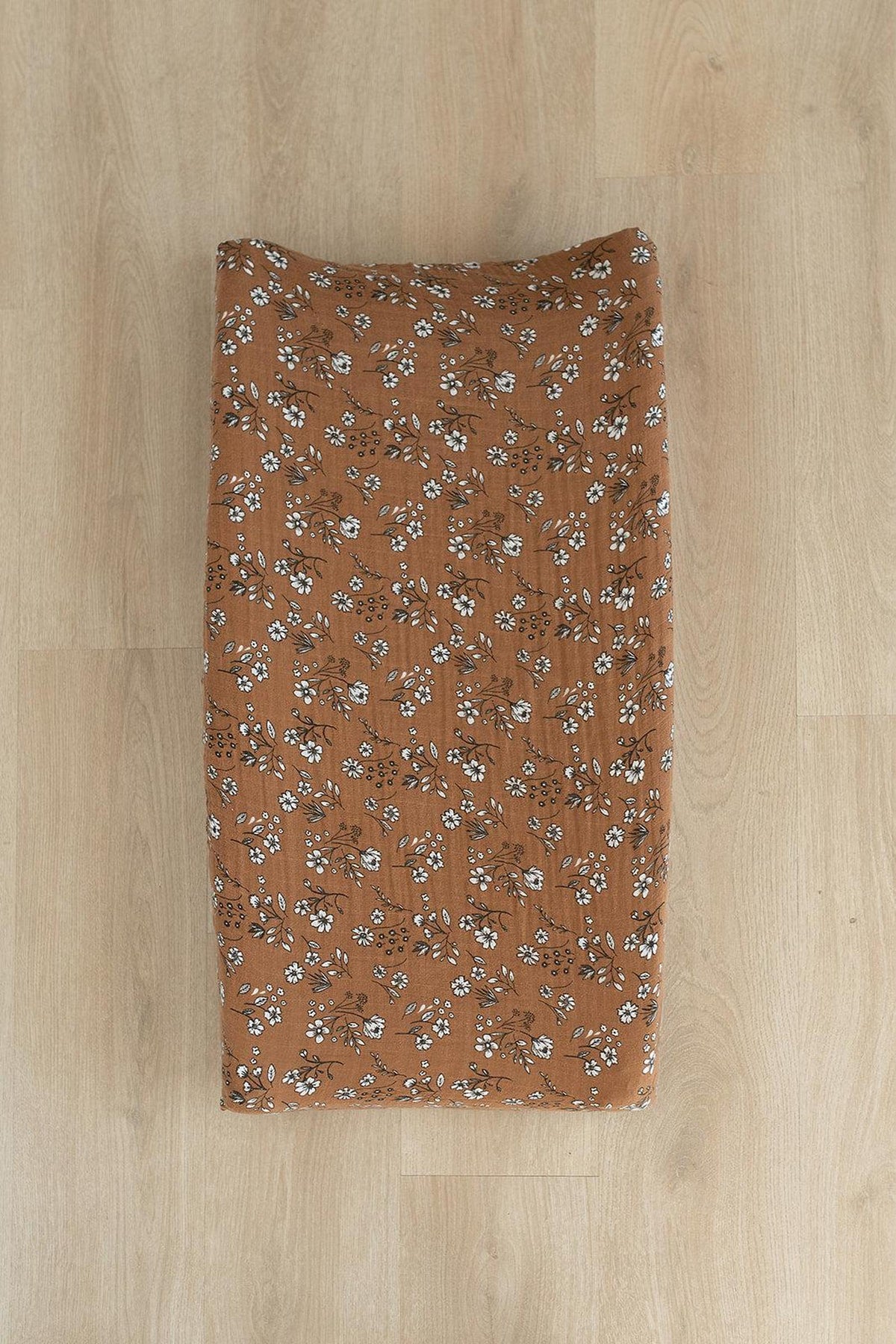 Brown changing pad cover with white floral pattern on a wooden floor, made from soft muslin cotton.