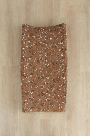 Brown changing pad cover with white floral pattern on a wooden floor, made from soft muslin cotton.