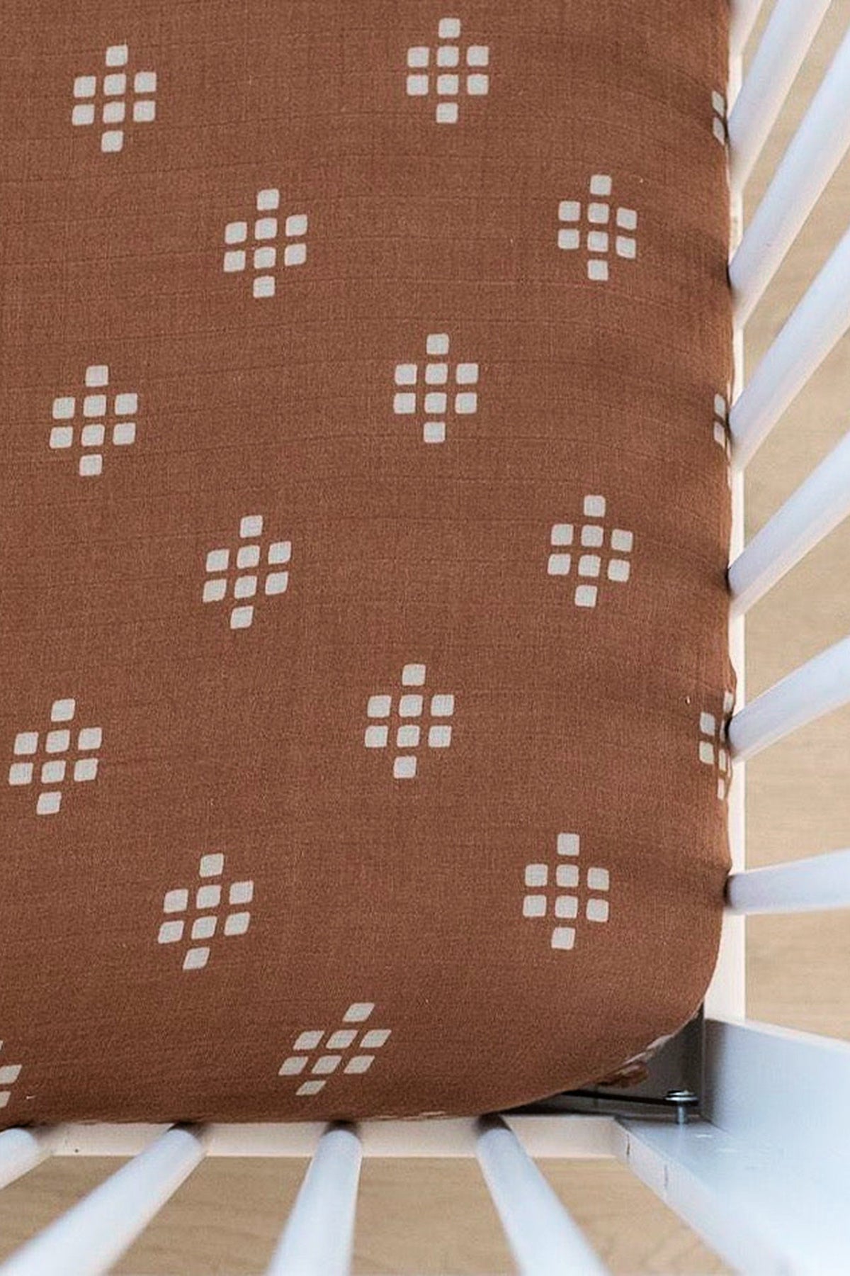 Brown muslin crib sheet with white geometric patterns on a white crib. Made from soft, breathable cotton.
