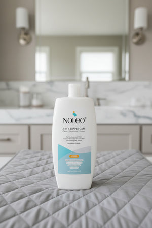 NOLEO 3-IN-1 Diaper Care bottle on a quilted gray surface in a modern bathroom setting.