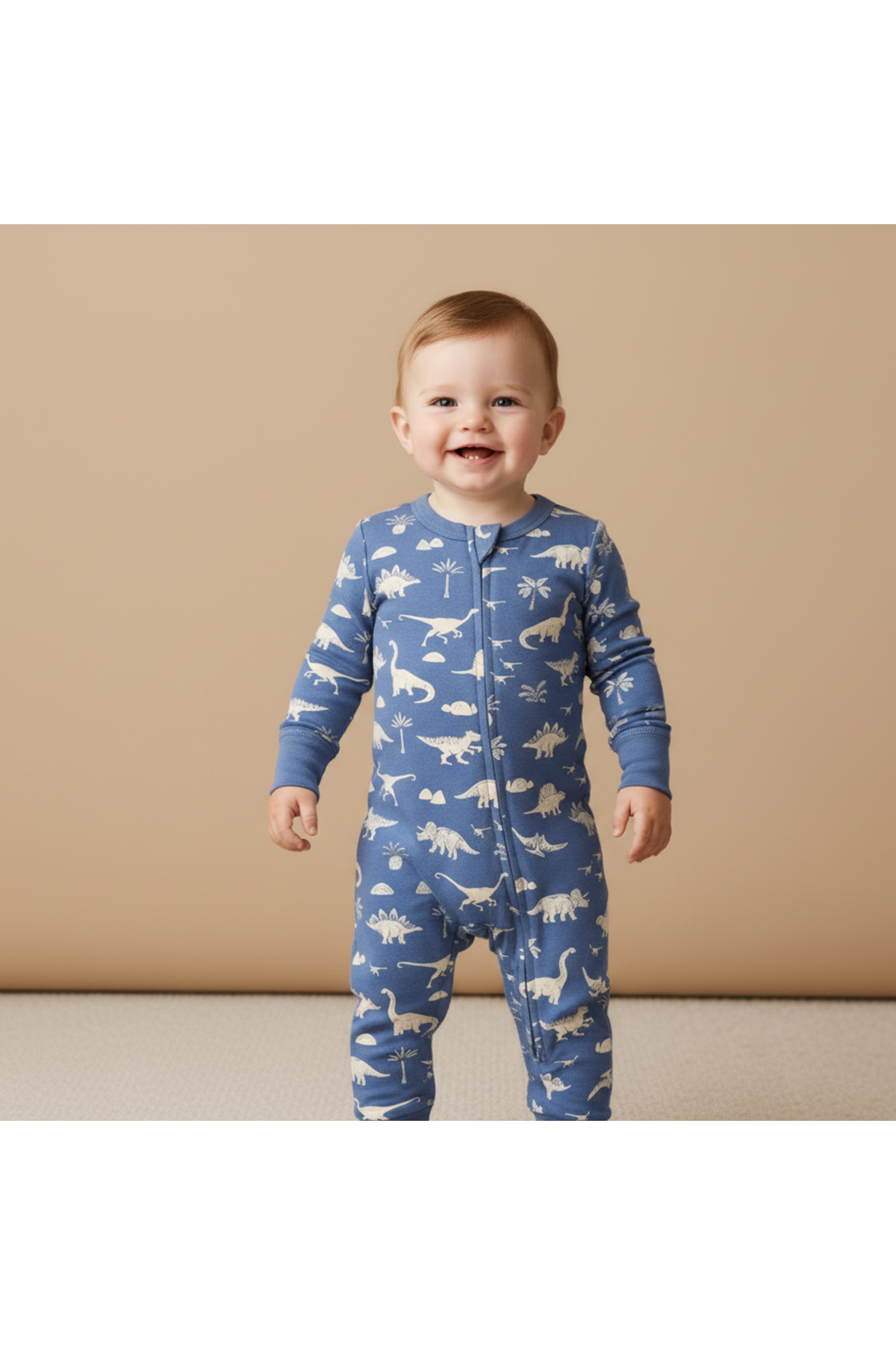 A smiling toddler stands in a blue organic cotton romper featuring white dinosaur prints. The romper has a two-way zipper and long sleeves, providing comfort and ease for everyday wear.