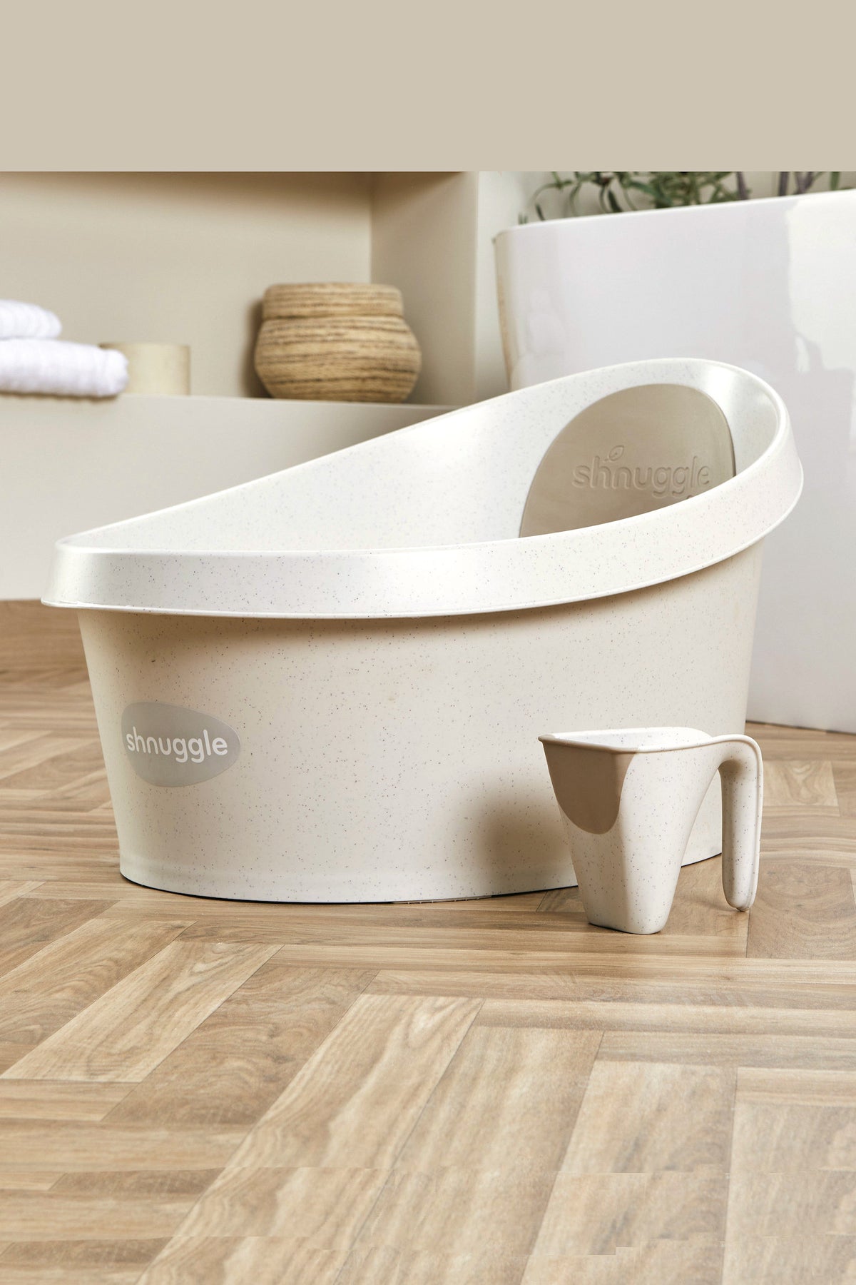 The image shows a Shnuggle Toddler Bath Tub in light beige with a matching jug on wooden flooring.