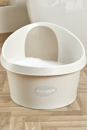 Cream-colored Shnuggle toddler bath tub with speckled texture and foam, set on a wooden floor.