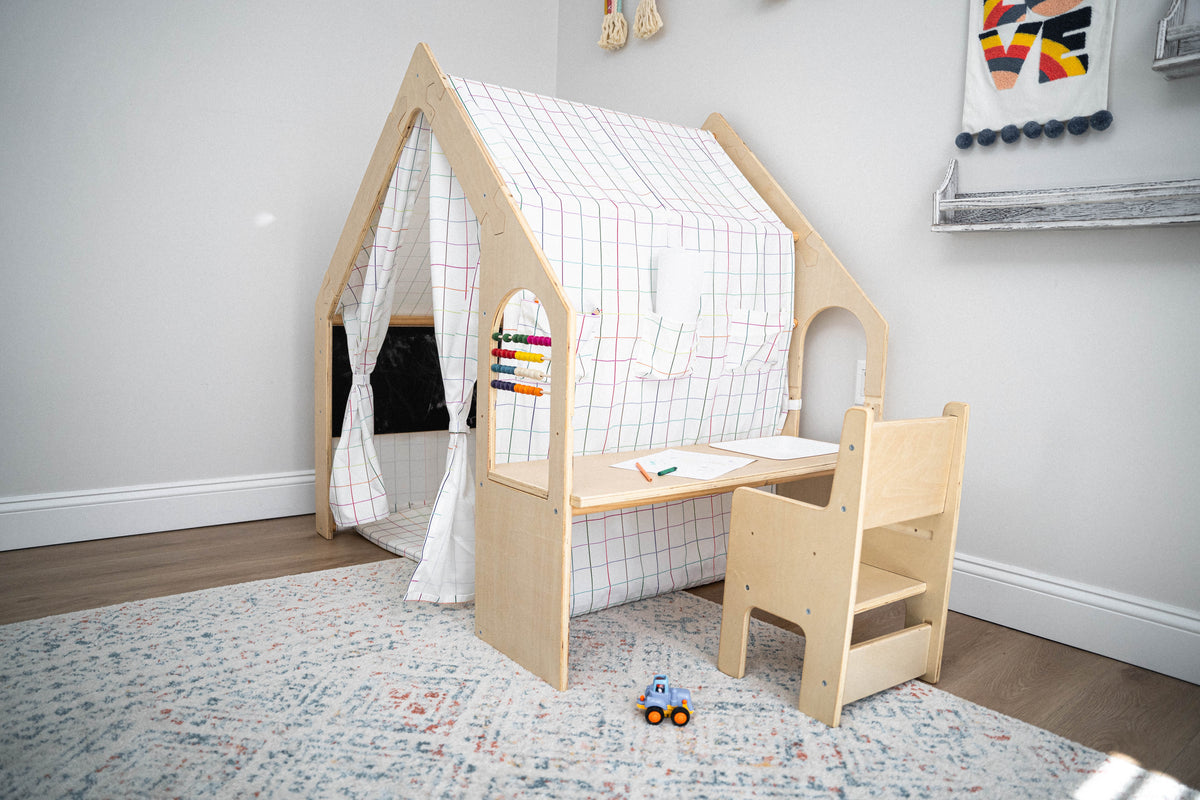 A wooden playhouse with a checkered fabric cover features a small desk and chair, creating a cozy space for children to play and learn. The setting is bright and inviting.