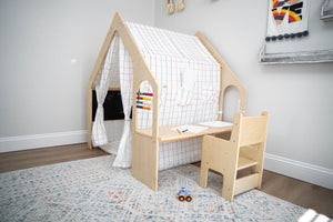 A wooden playhouse with a checkered fabric cover features a small desk and chair, creating a cozy space for children to play and learn. The setting is bright and inviting.