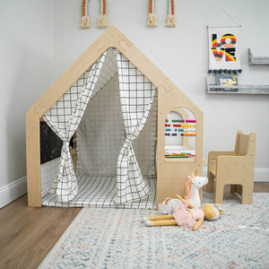 A wooden playhouse with a grid-patterned curtain features an adjacent sensory desk with colorful beads and a chair. Plush toys are scattered on a soft area rug nearby.