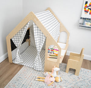 A wooden playhouse features a grid-patterned canopy and a small desk with a chair. Colorful beads and a plush toy are placed nearby, creating a cozy play environment for children.