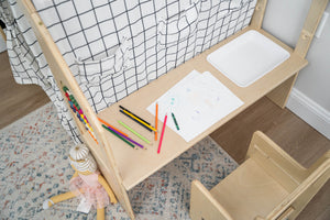 A wooden desk with a simple design features a white drawing surface, surrounded by colorful art supplies. Nearby, a small chair and a doll add to the inviting play space.