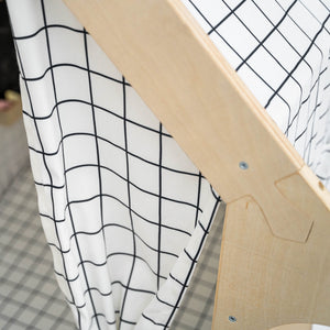 A close-up of a playhouse featuring a white fabric with a black grid pattern, draped over a natural wooden frame.