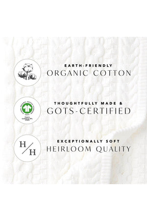 A close-up of a textured white fabric with a cable knit pattern, featuring labels indicating it is made from organic cotton, GOTS-certified, and of heirloom quality.