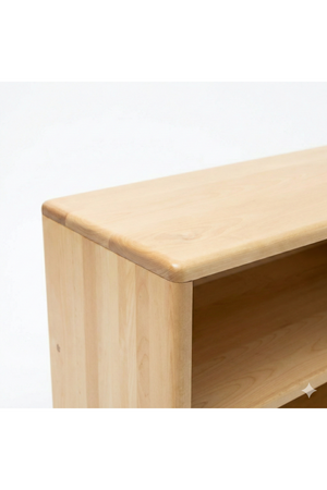 A close-up view of a smooth, light-colored wooden shelf edge, showcasing its rounded corners and natural finish. The shelf is part of a larger Montessori toy and book organizer.