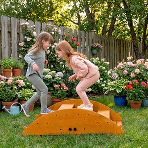 Two children play joyfully on a wooden Jumbo Rocker and Climber in a vibrant garden filled with colorful flowers, showcasing outdoor active play in a natural setting.