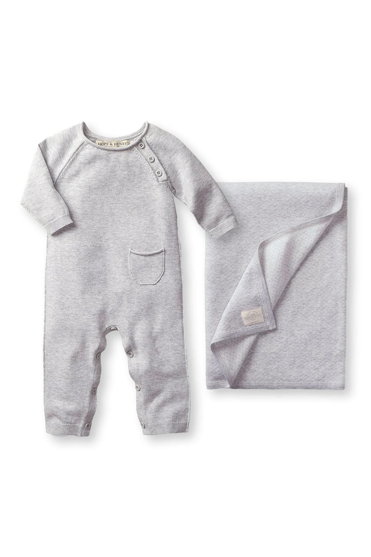 A gray organic cotton romper with a pocket and buttons is displayed alongside a matching jacquard blanket.