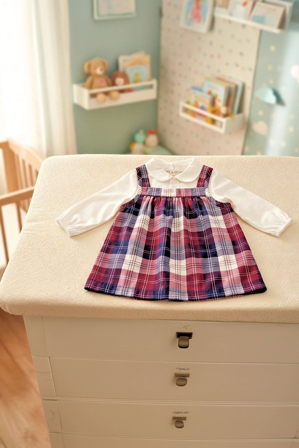 A long-sleeve white bodysuit with a Peter Pan collar is paired with a berry tartan plaid jumper, displayed neatly on a soft surface.